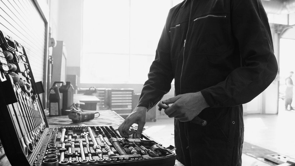 Mechanic in overalls selects a tool from an open toolbox in a workshop.