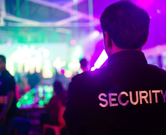 A security guard is standing in front of a crowd at a party.