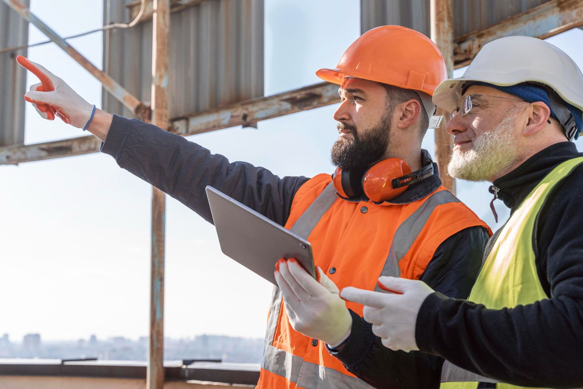 Two construction workers are looking at a tablet on a construction site.