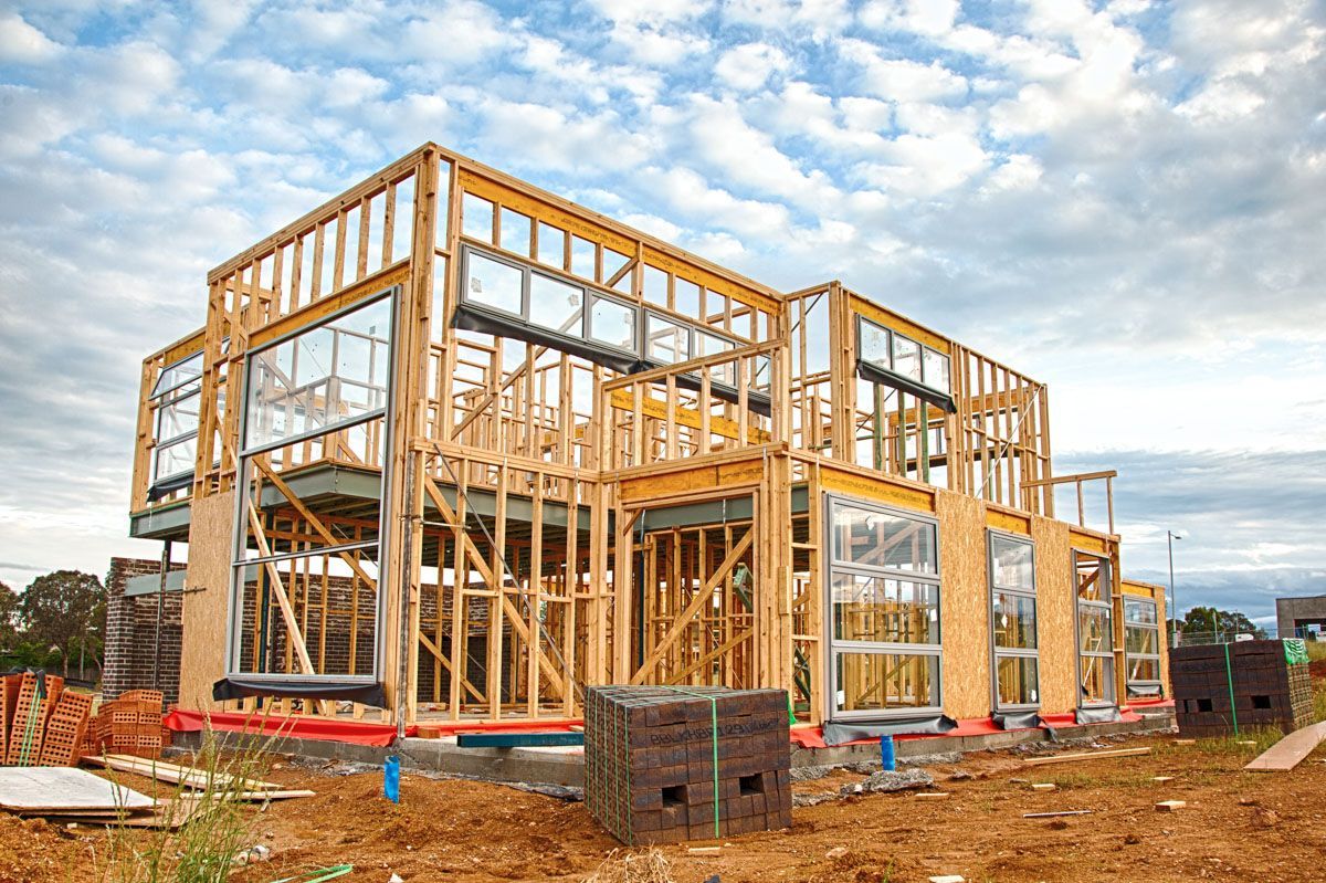 A large wooden house is being built in a dirt field.