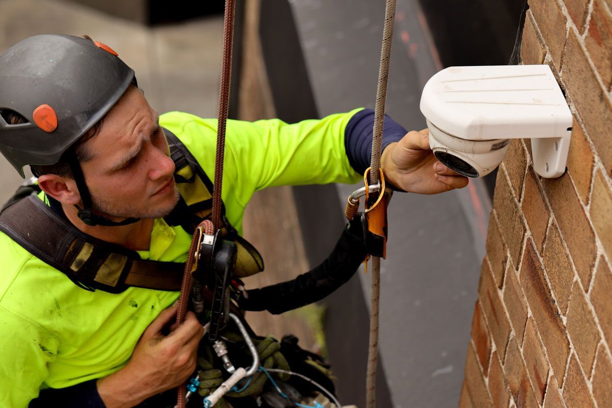 A man wearing a helmet is working on a camera on a brick wall.