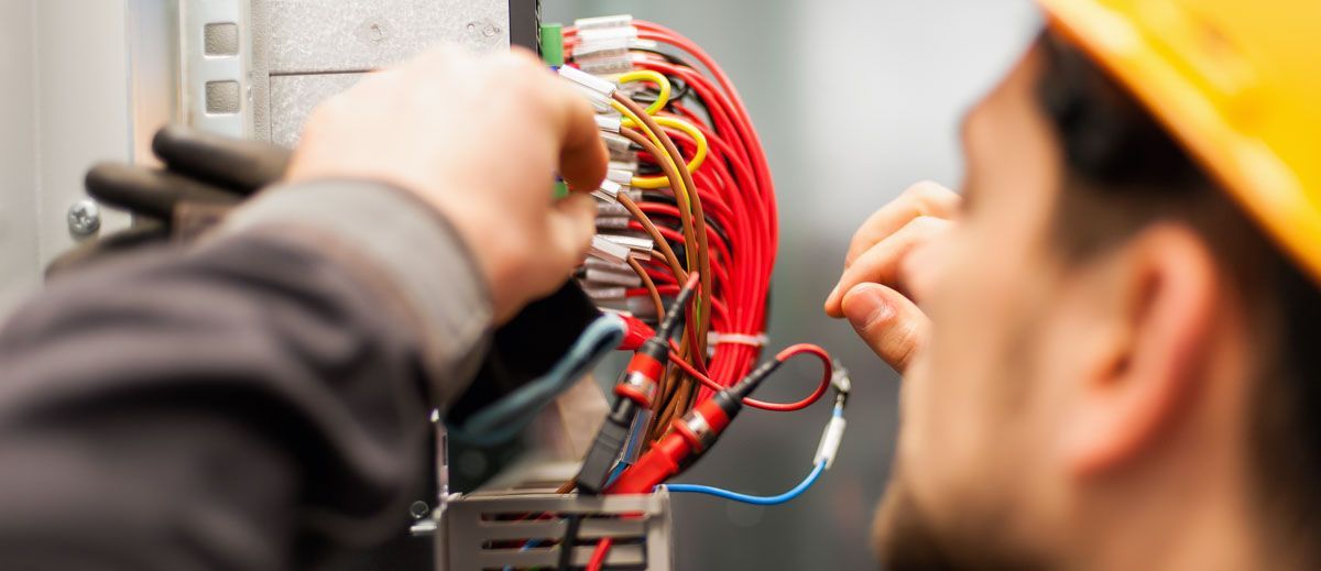A man wearing a hard hat is working on an electrical box.