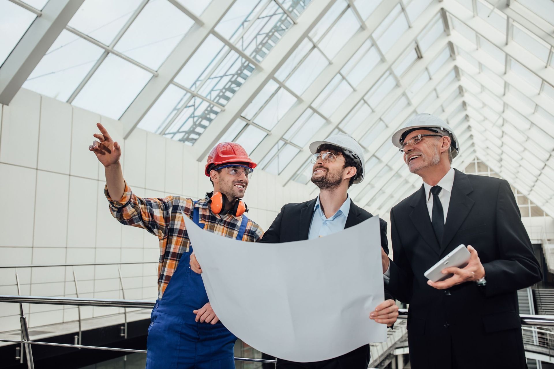 Three men are standing next to each other in a building looking at a blueprint.