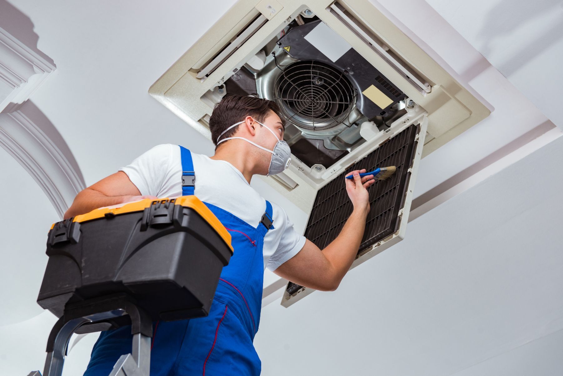 A man wearing a mask is working on an air conditioner.