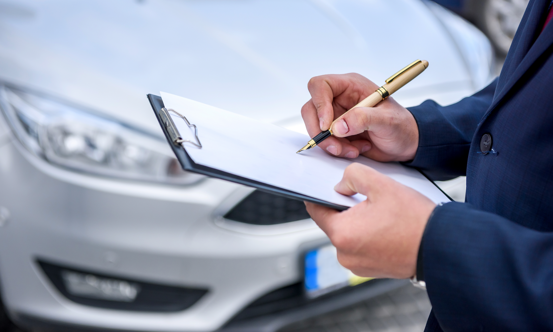 A man is writing on a clipboard in front of a car.