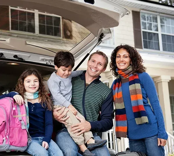 Family smiles in front of car's open trunk, ready for travel, sunny day.