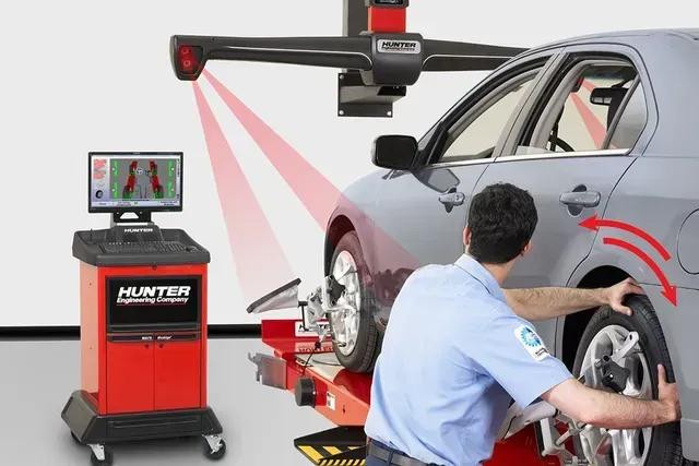 A technician aligns a gray car's wheels using a red Hunter alignment machine.