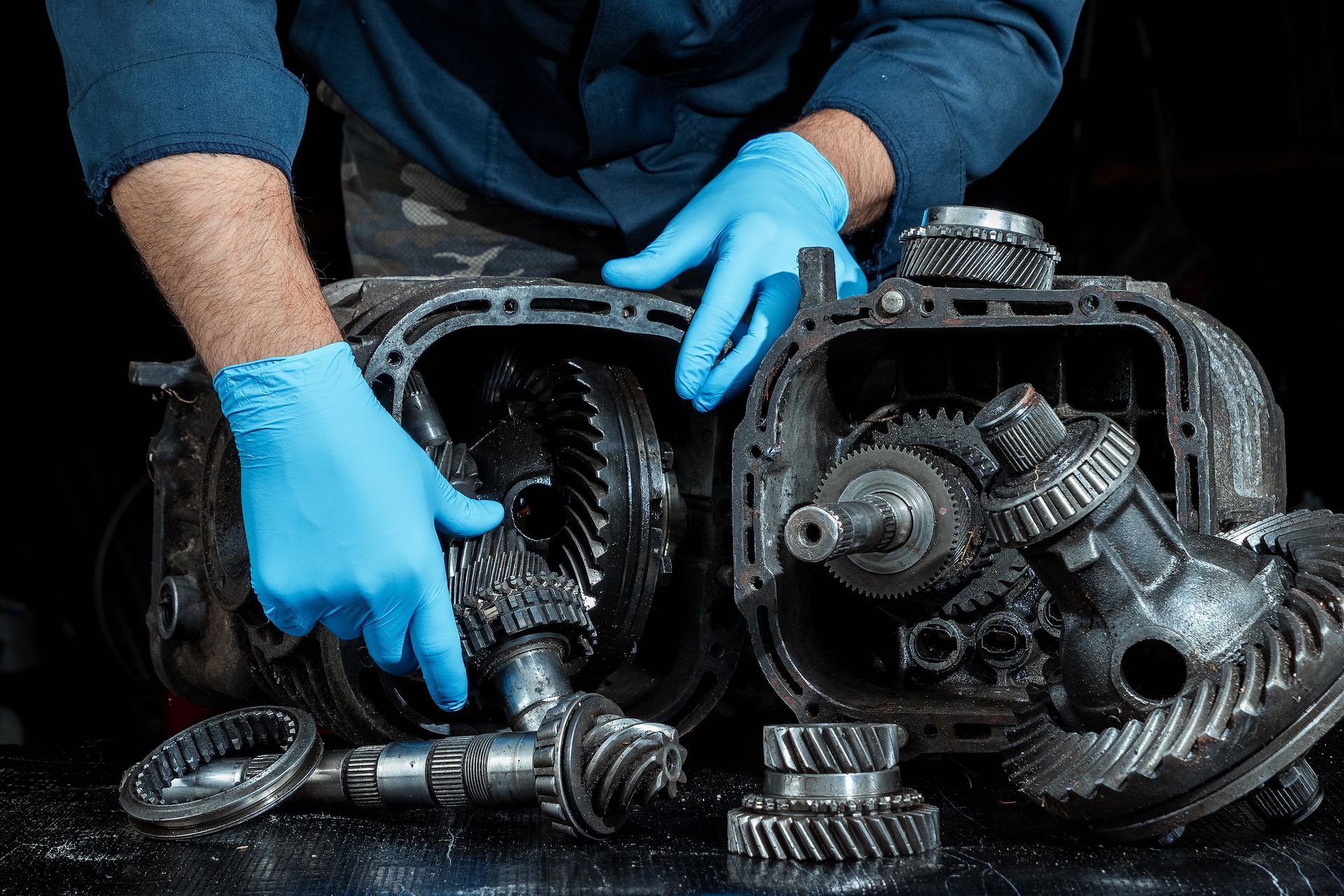 A man wearing blue gloves is working on a gearbox.