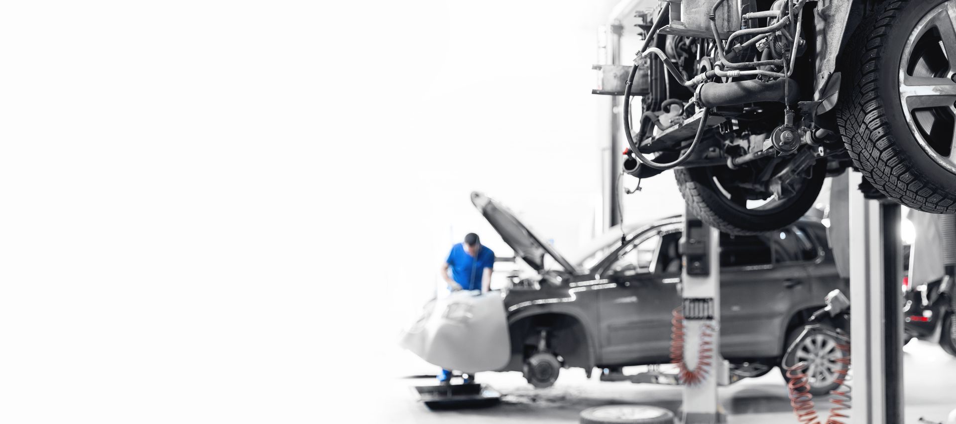 A man is working on a car in a garage with the hood open.