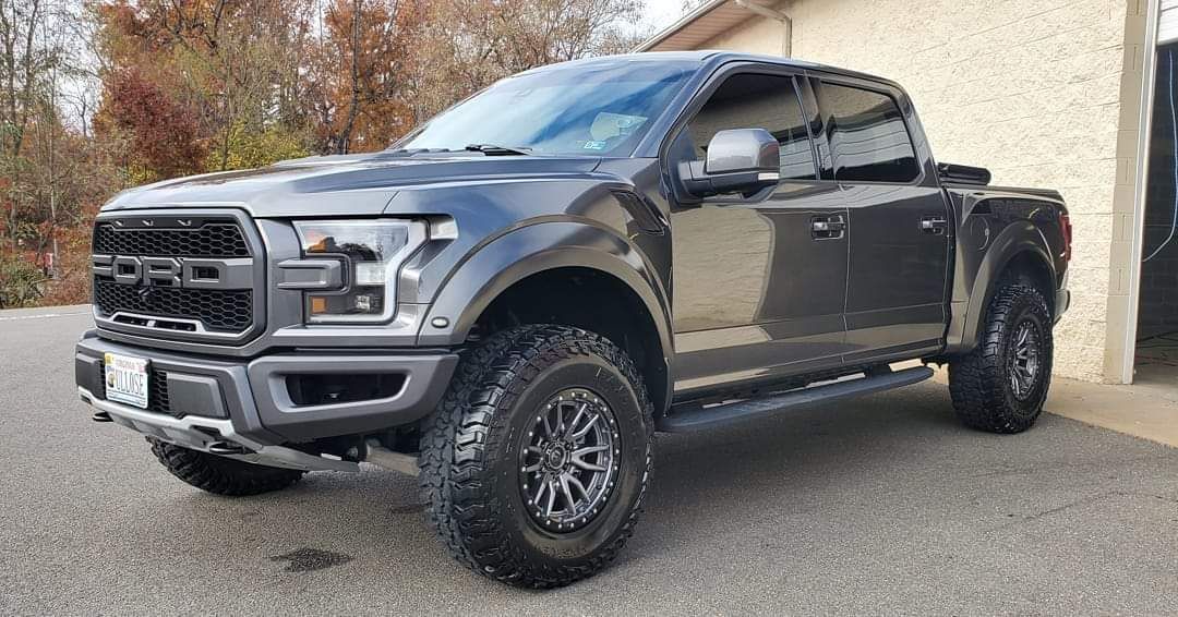A black ford raptor truck is parked in front of a house.
