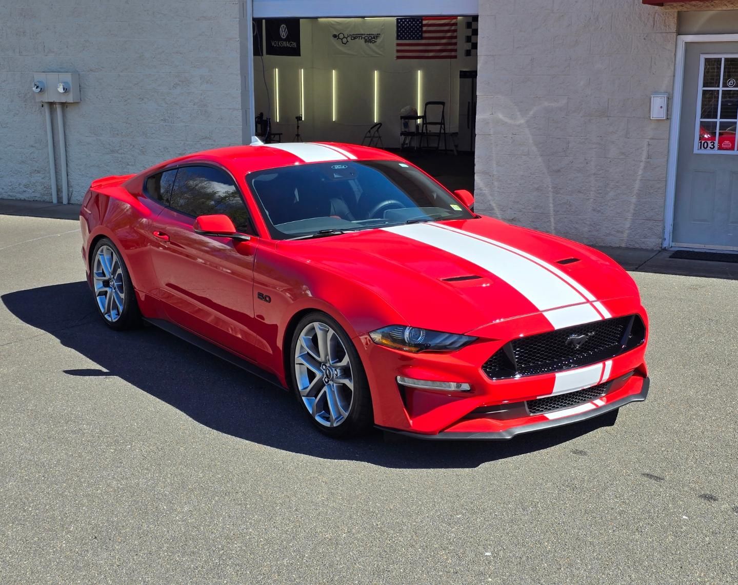 A red mustang is parked in front of a garage