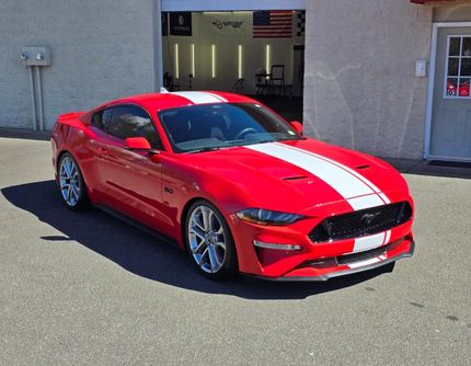 A red mustang with white stripes is parked in front of a garage.