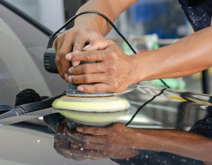 A man is polishing the hood of a car with a machine.