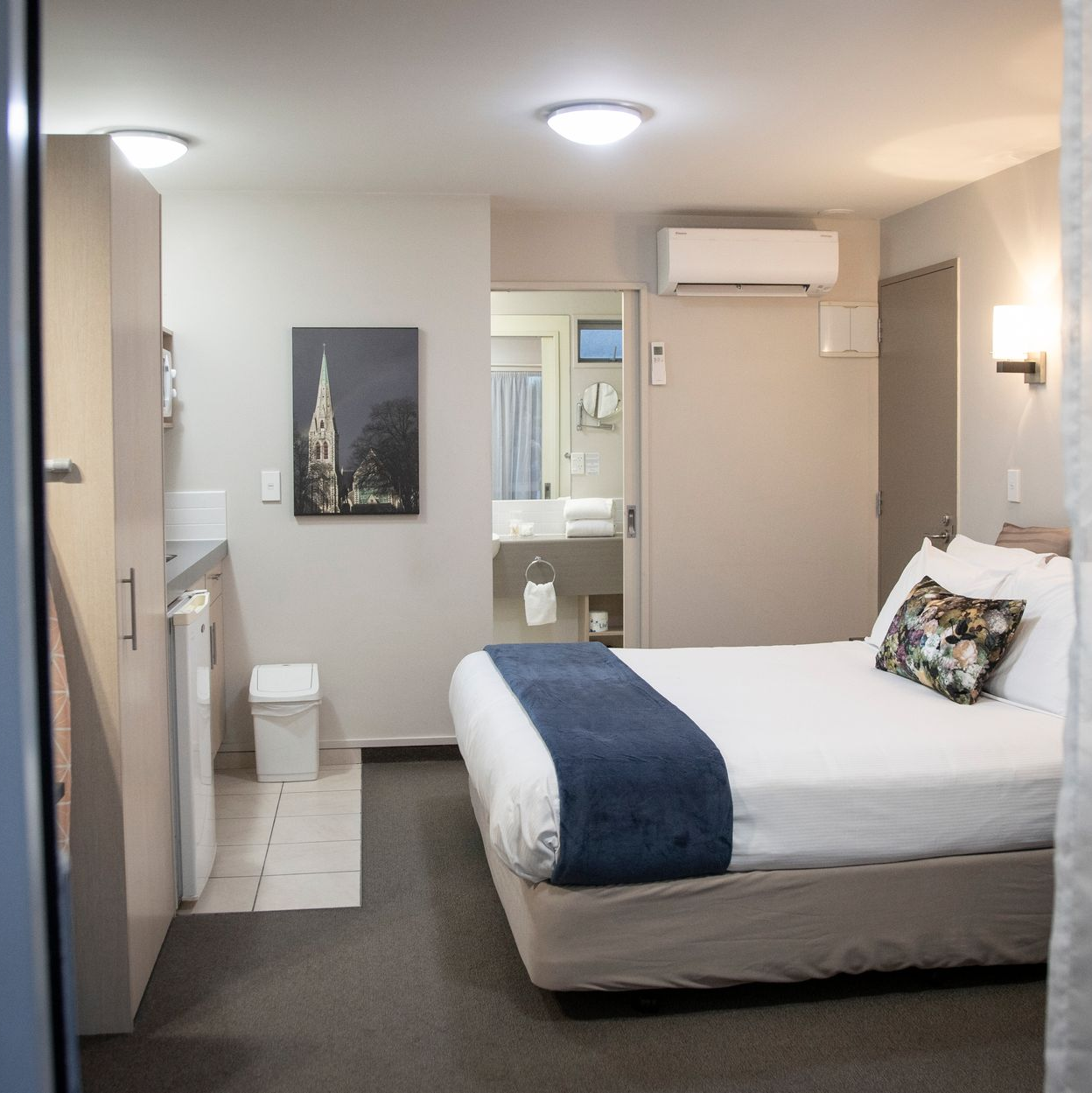 Two beds in a hotel room with red bedspreads, pillows, and side tables.