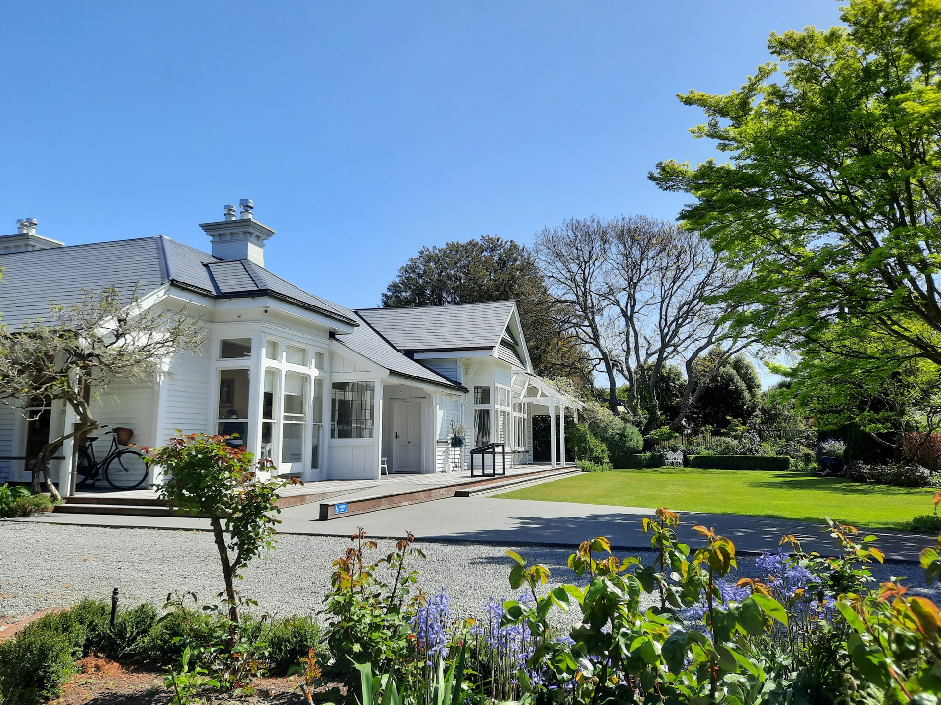 White Victorian house with a gray roof, set in a garden under a blue sky.