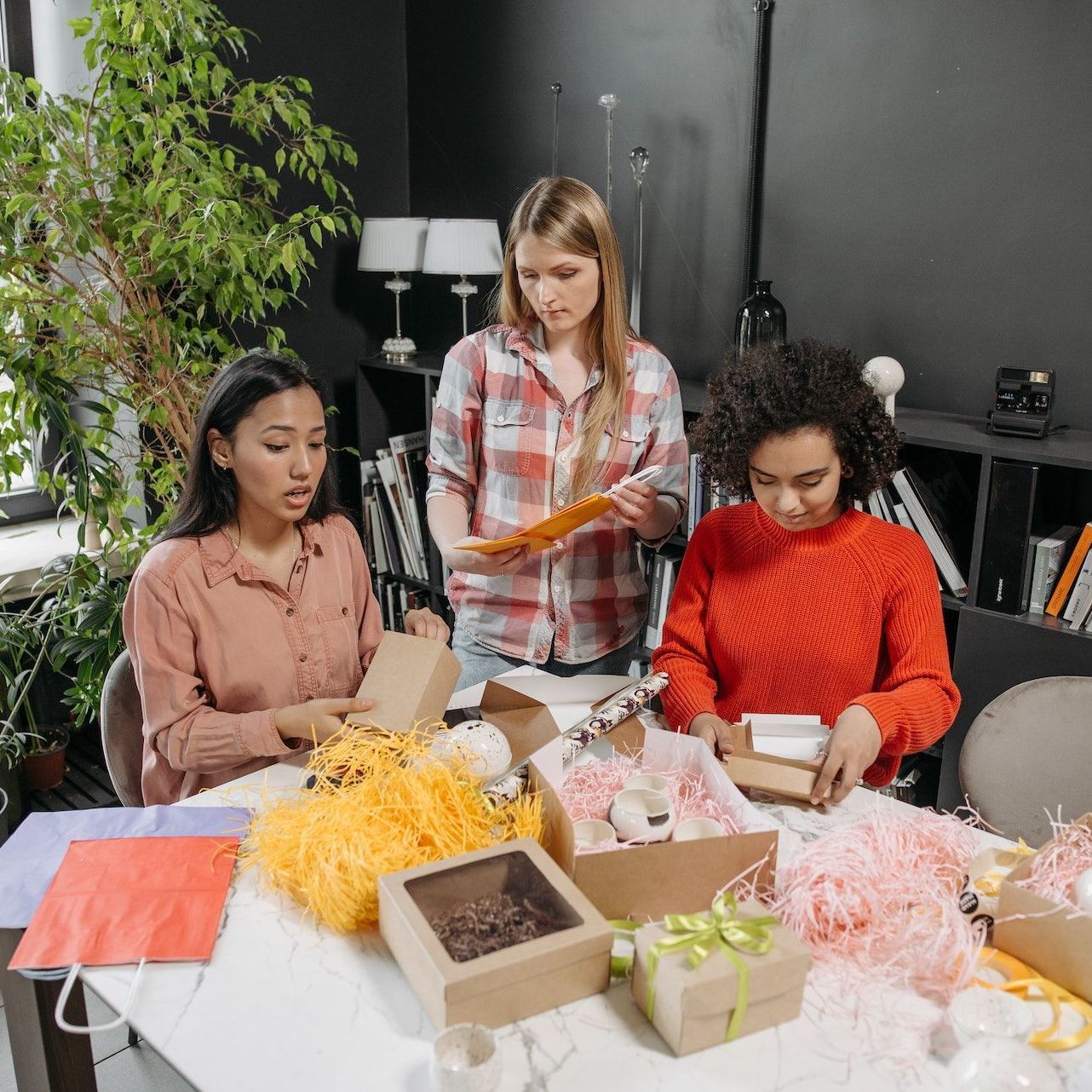 Three women are sitting at a table wrapping gifts.