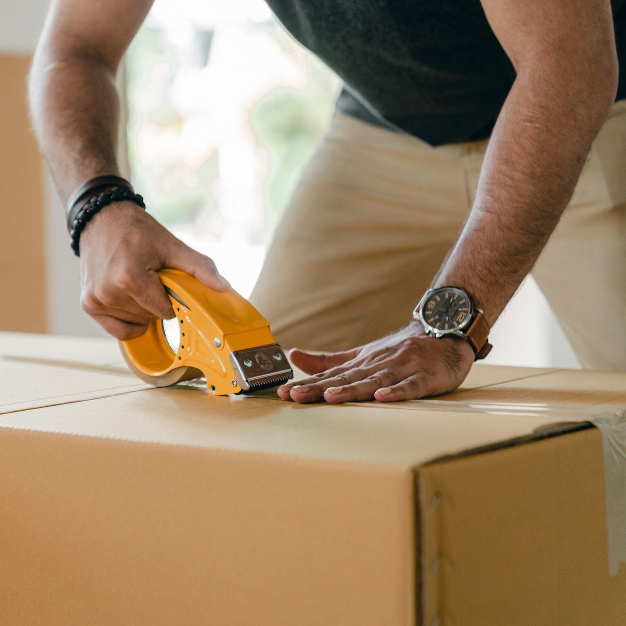 A man wearing a watch is taping a cardboard box