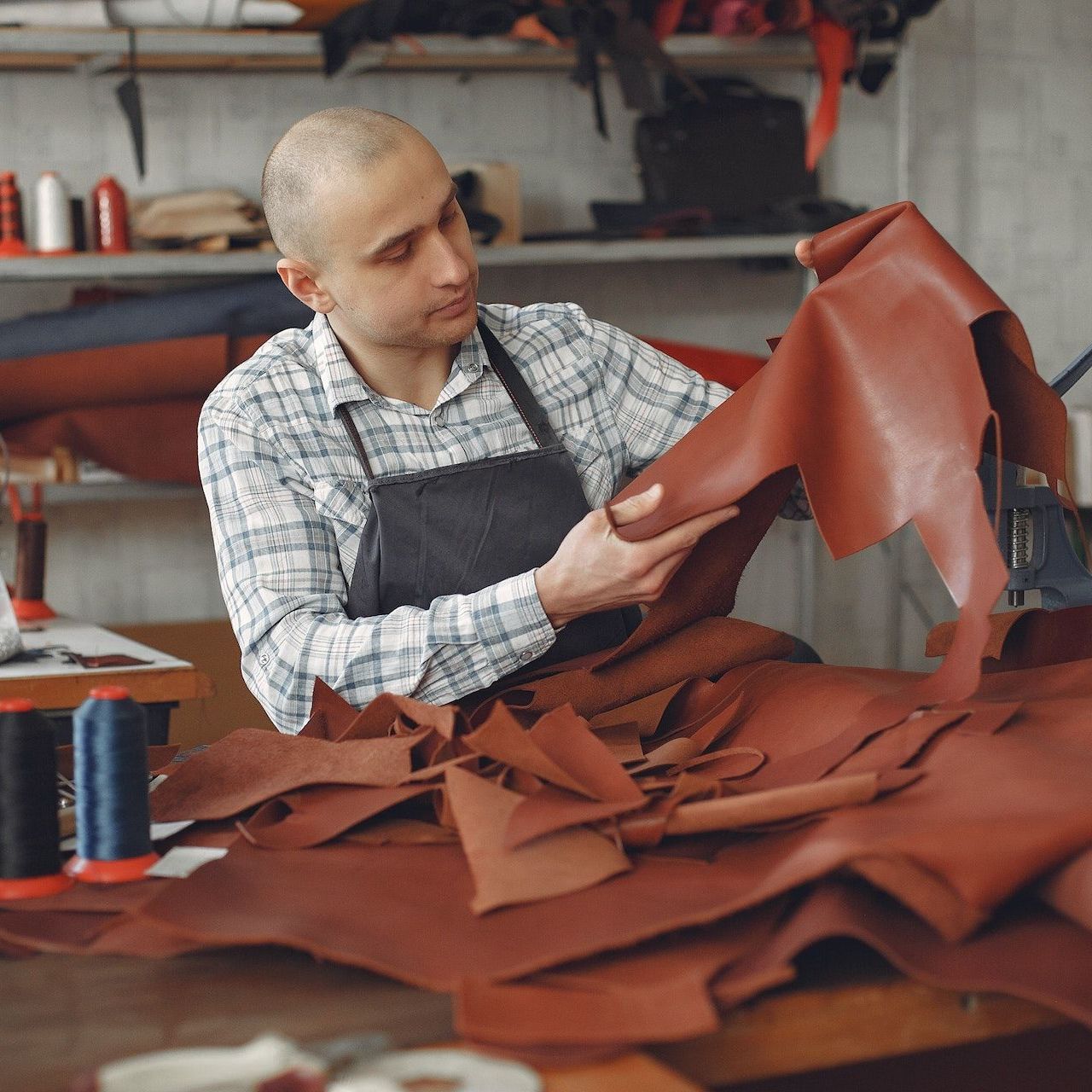 A man in an apron is holding a piece of brown leather