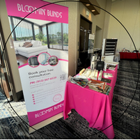 A table with a pink tablecloth and a sign that says bloomin blinds on it.
