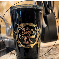 A black tumbler with the words `` bootleg bourbon balls '' on it is sitting on a counter.