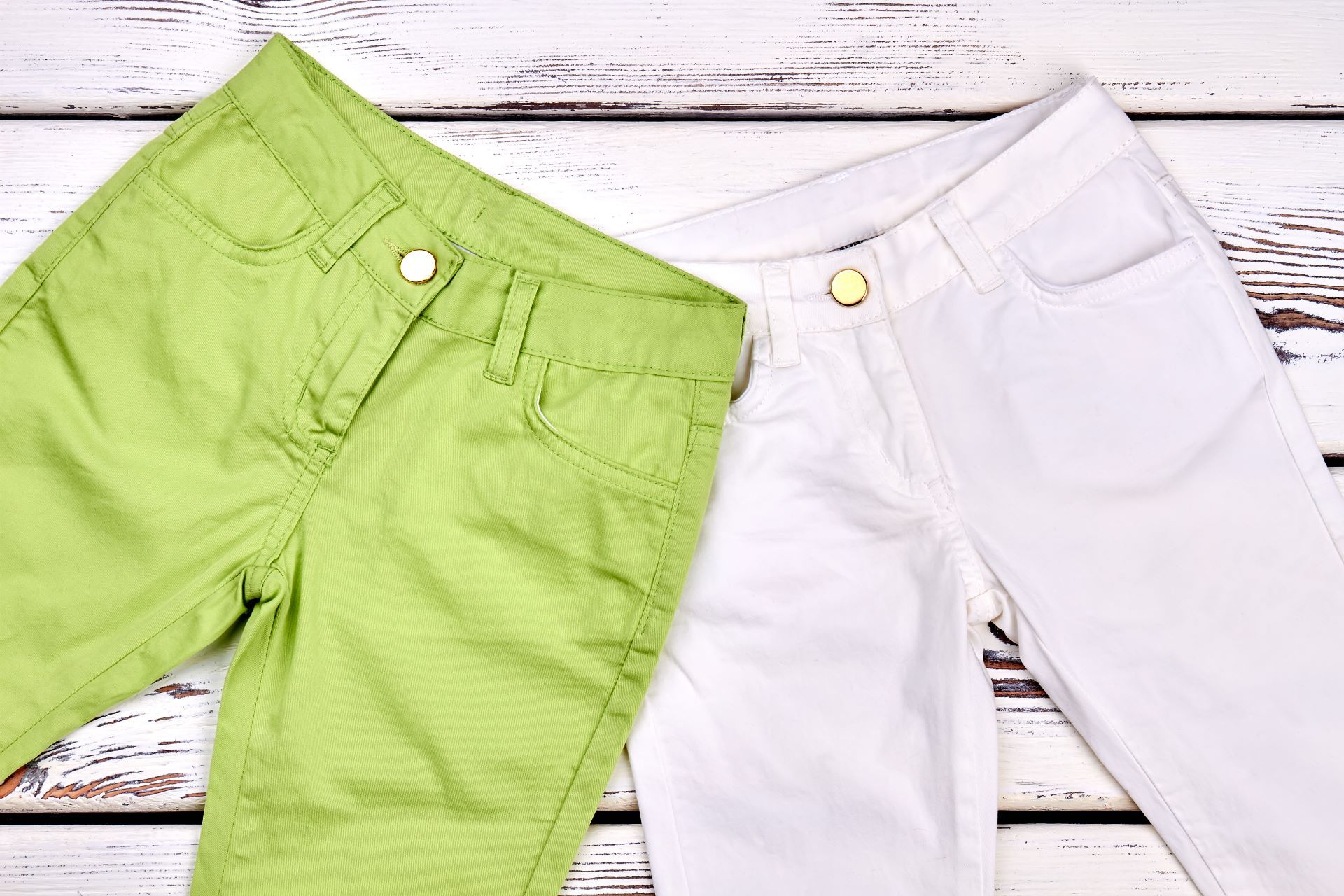 Two pairs of pants , one green and one white , are sitting on a wooden table.
