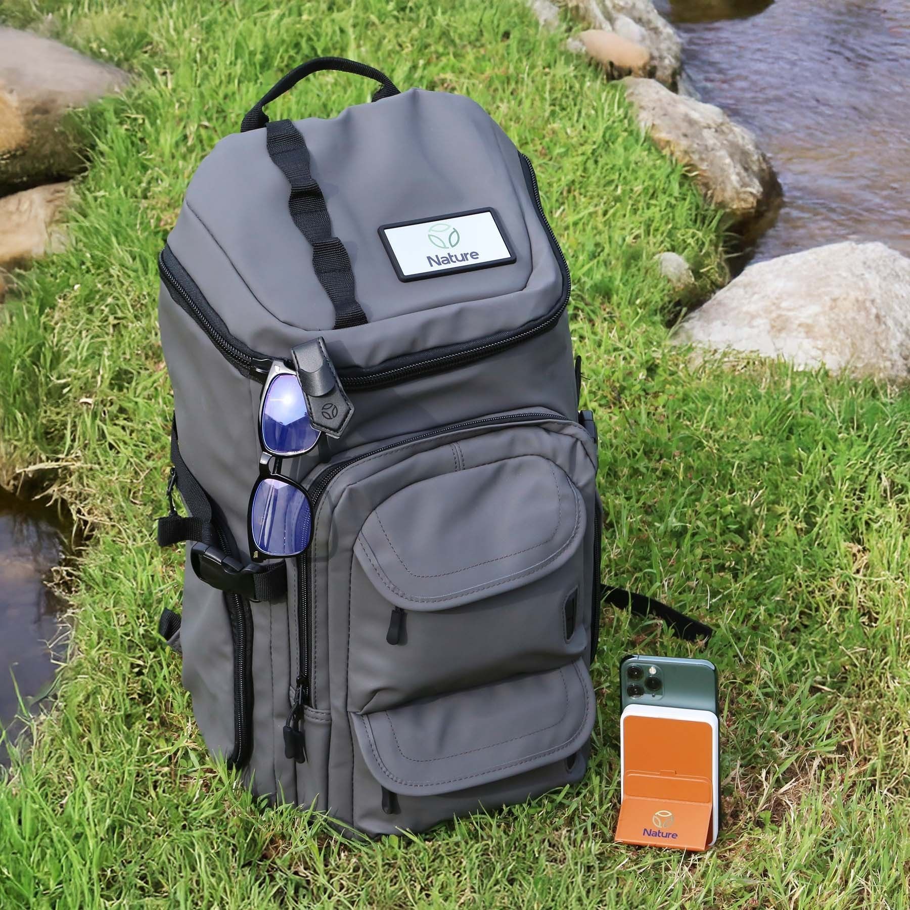 A gray backpack is sitting in the grass near a stream