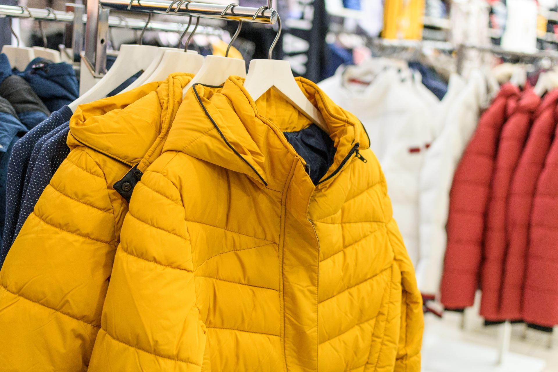 A yellow padded jacket with a hood is hanging on a rack in a store.