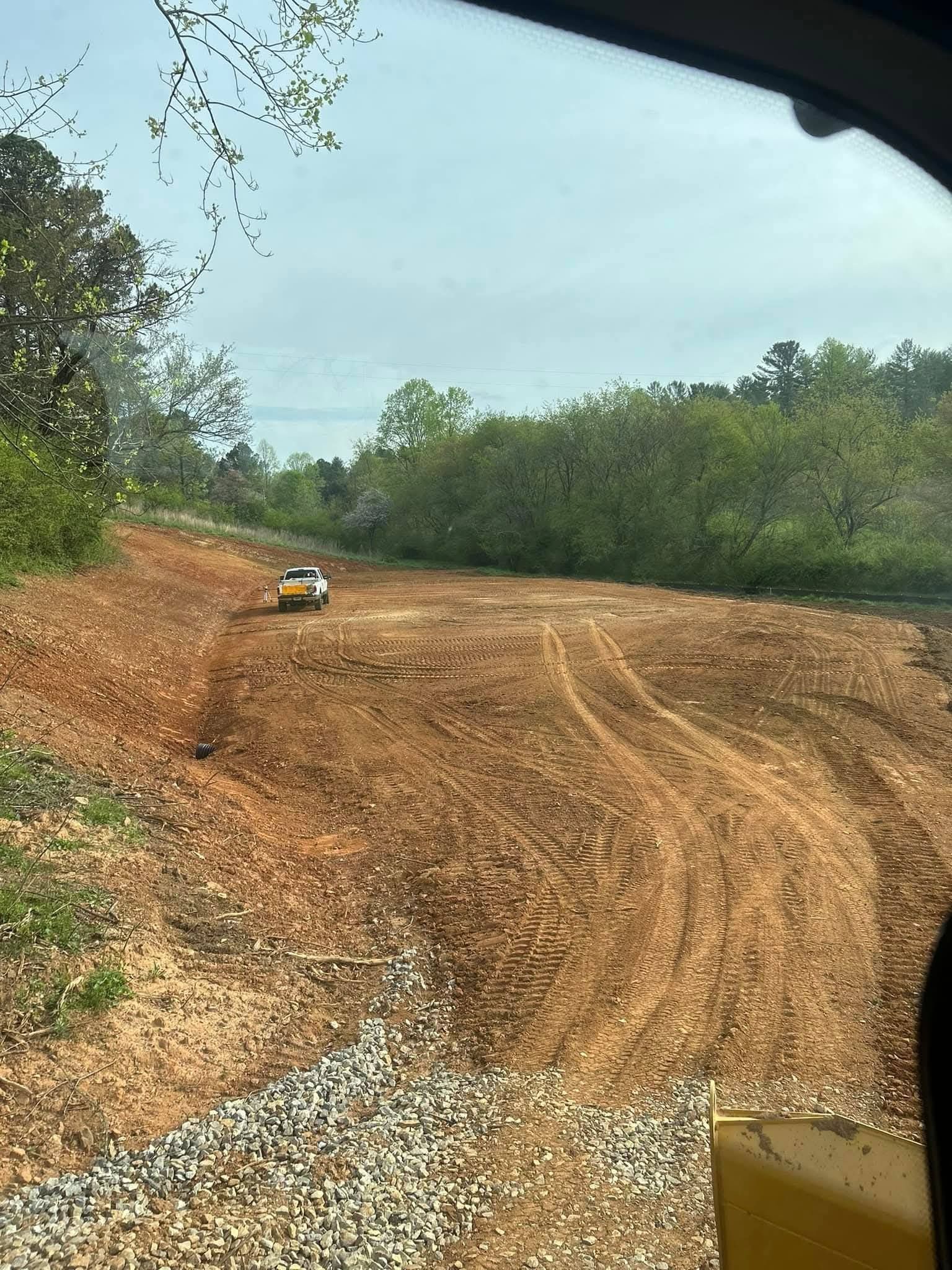 A white pickup truck parked on a cleared, muddy construction site with tire tracks near a tree line.