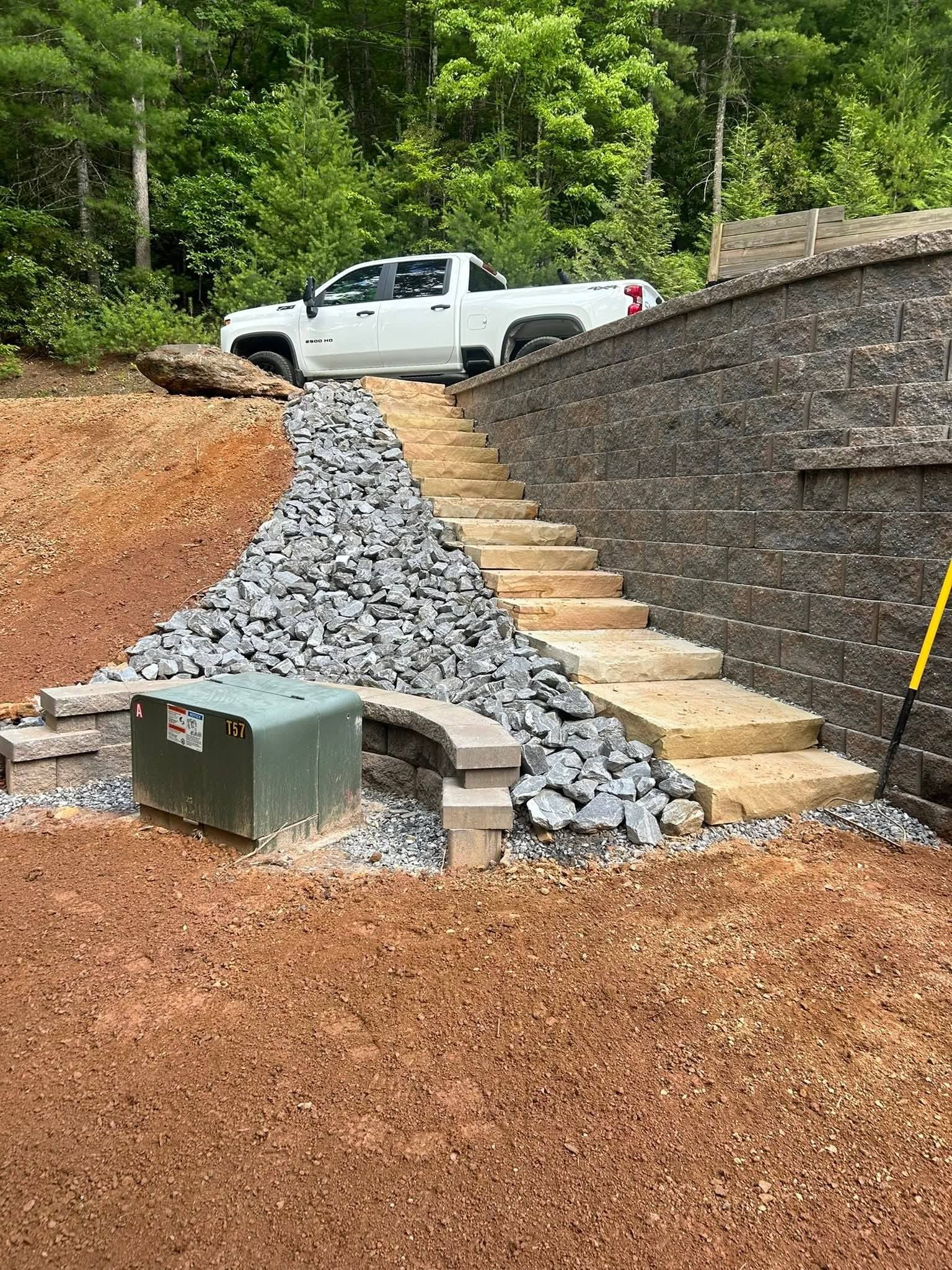 A white pickup truck parked above a new stone retaining wall with matching steps alongside a bed of gray gravel.