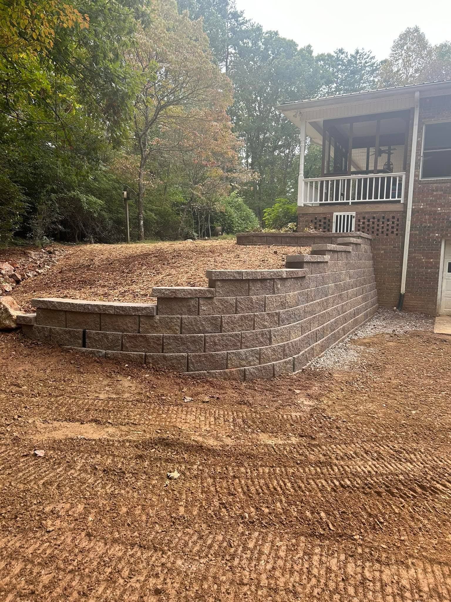 A newly installed tiered stone retaining wall in front of a house, surrounded by a yard covered in fallen leaves.