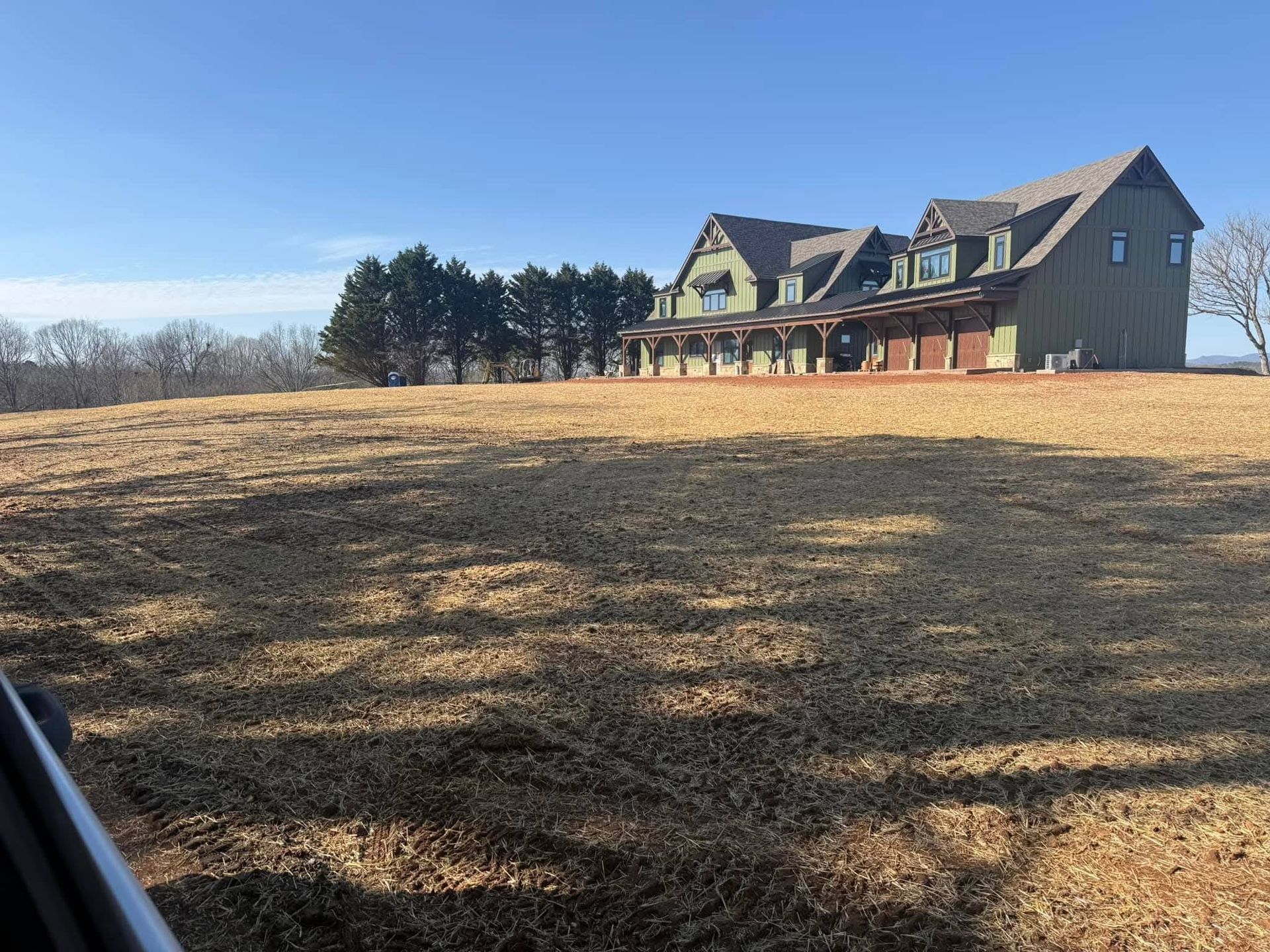 A large, multistory house with a brown exterior stands on a grassy hill under a clear blue sky.