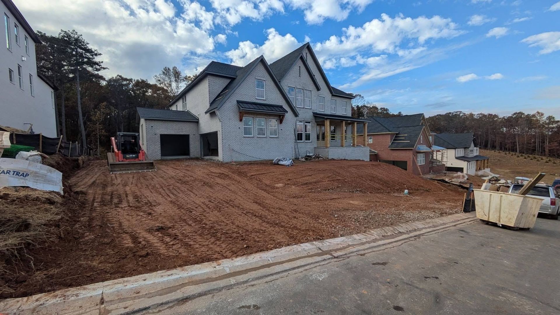 A new two-story house under construction with light-colored siding, a dark roof, and a large, unfinished dirt front yard.