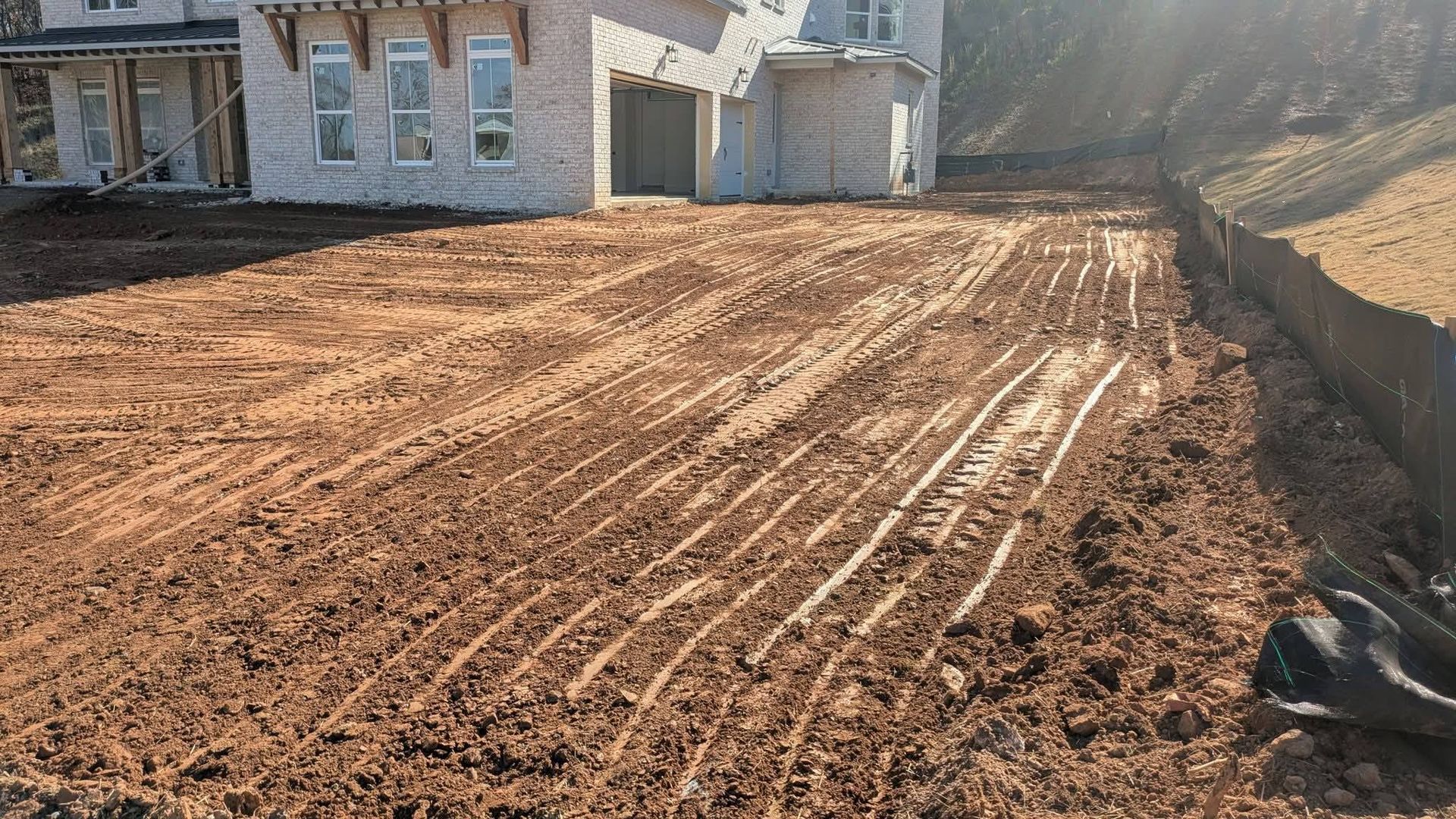 A freshly graded dirt yard with visible tire tracks in front of a house under construction.