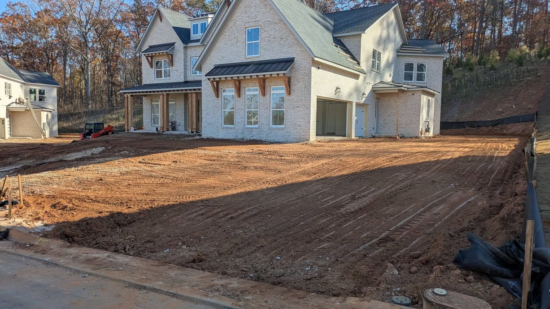 Newly constructed, multi-story brick house with a large, unfinished dirt front yard under a bright, clear blue sky.