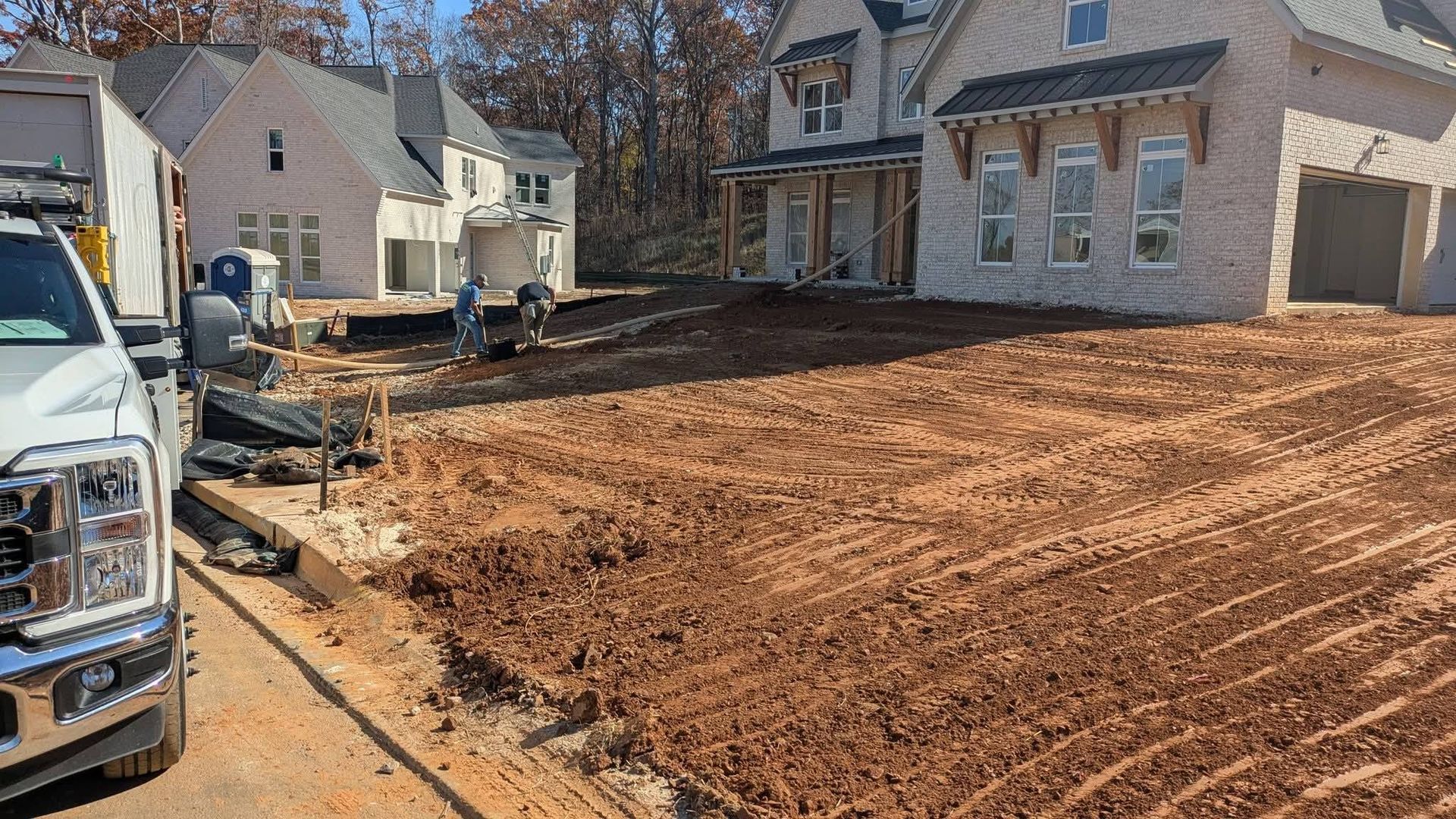 A white truck is parked near a construction site featuring new houses and a large, freshly graded dirt yard.