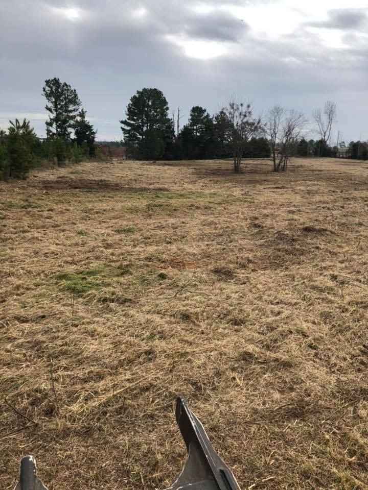 A view from a tractor looking over a large, dry field toward a line of trees under a cloudy sky.