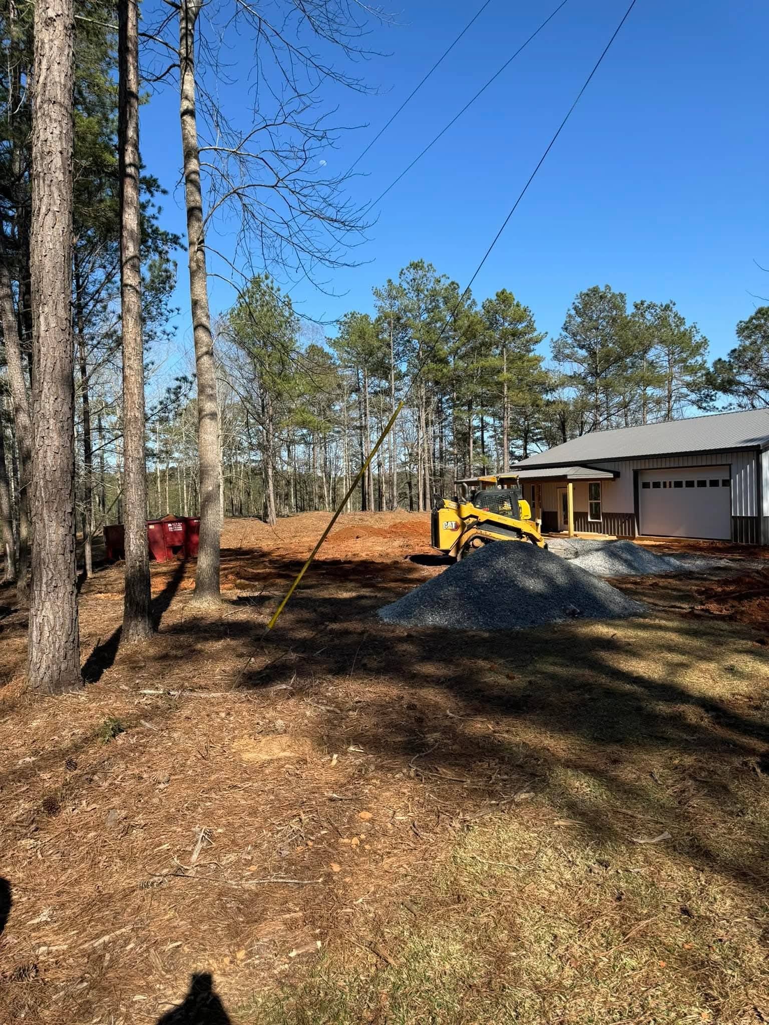 A yellow bulldozer sits on a cleared, dirt construction site next to a garage and piles of gravel under a clear sky.