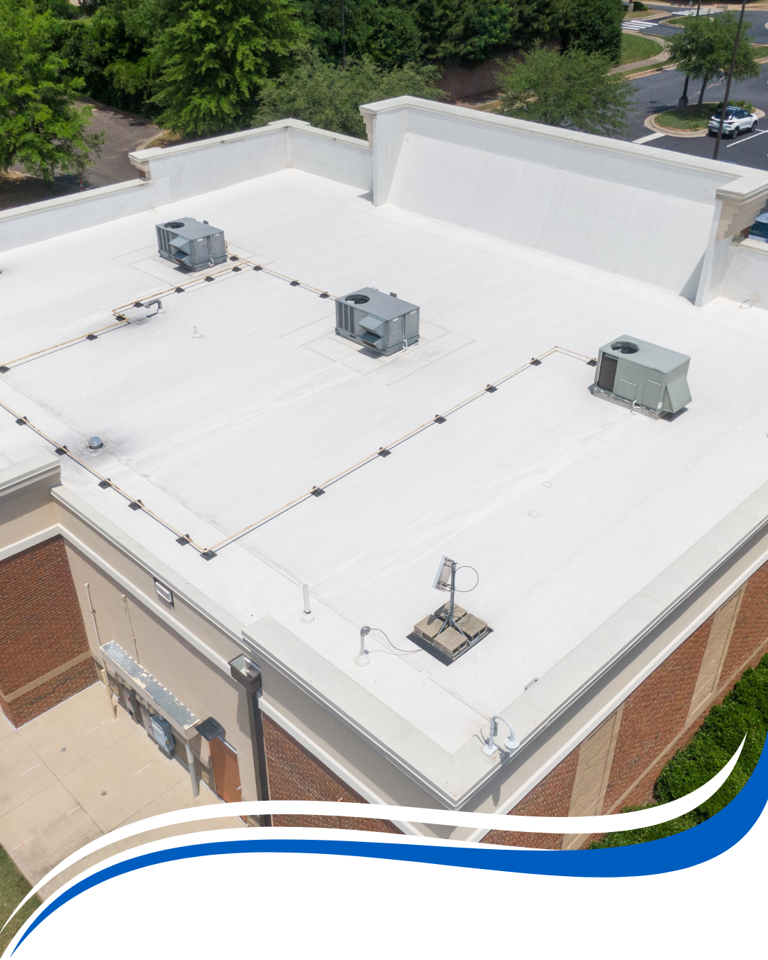 An aerial view of a commercial building's white flat roof with several HVAC units and electrical wiring.