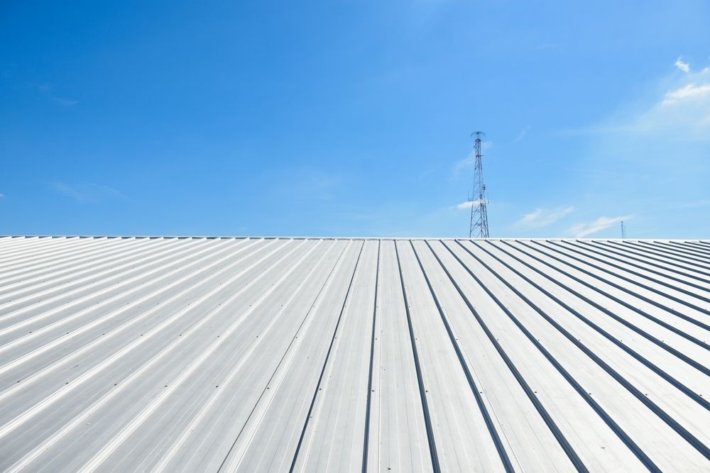 Silver corrugated metal roof under a bright blue sky, with a distant utility tower.