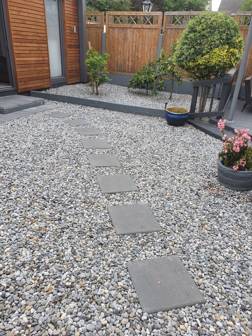 A garden with gravel , stepping stones , flowers and a fence.