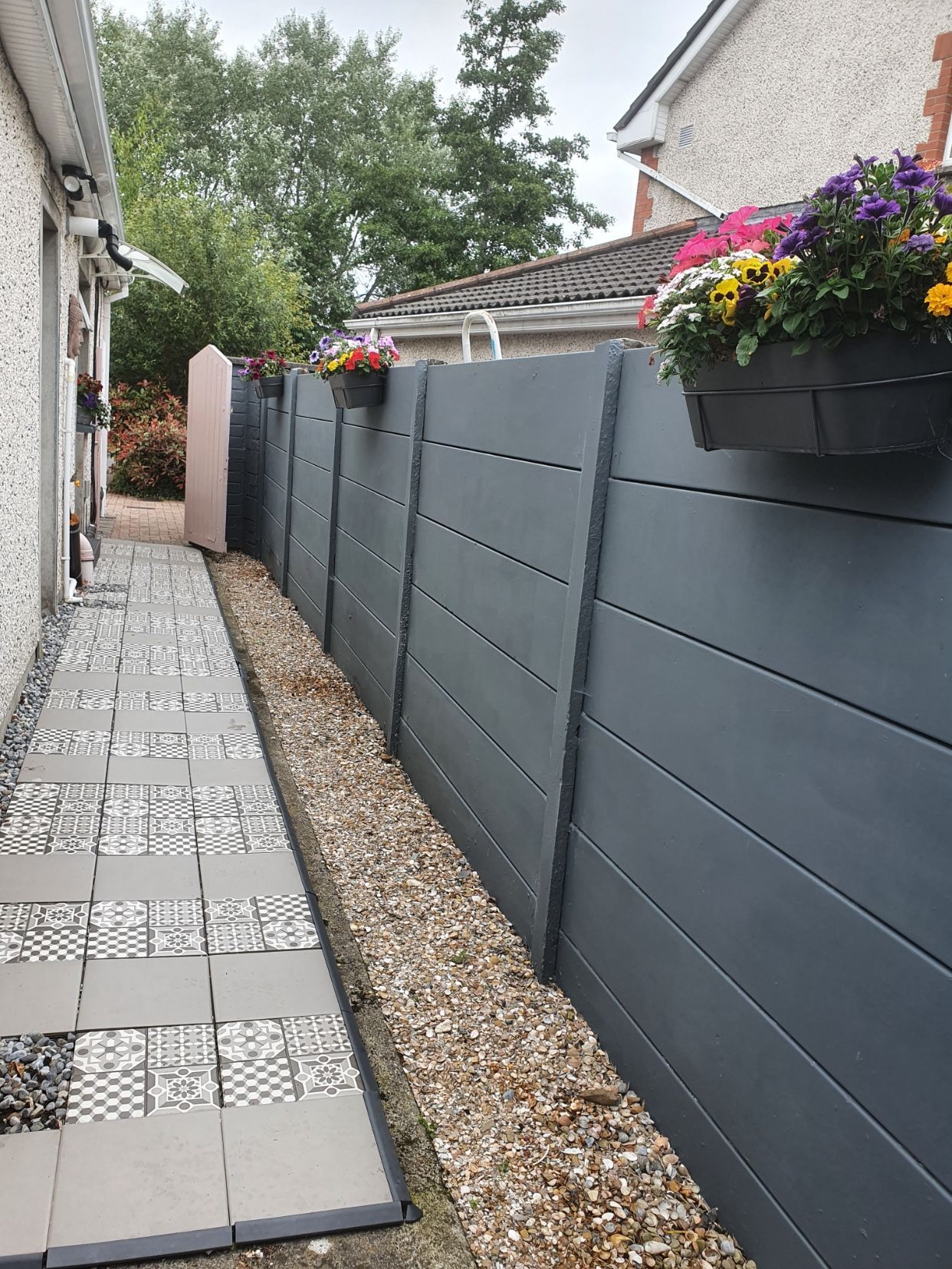 A fence with flowers hanging from it next to a sidewalk.