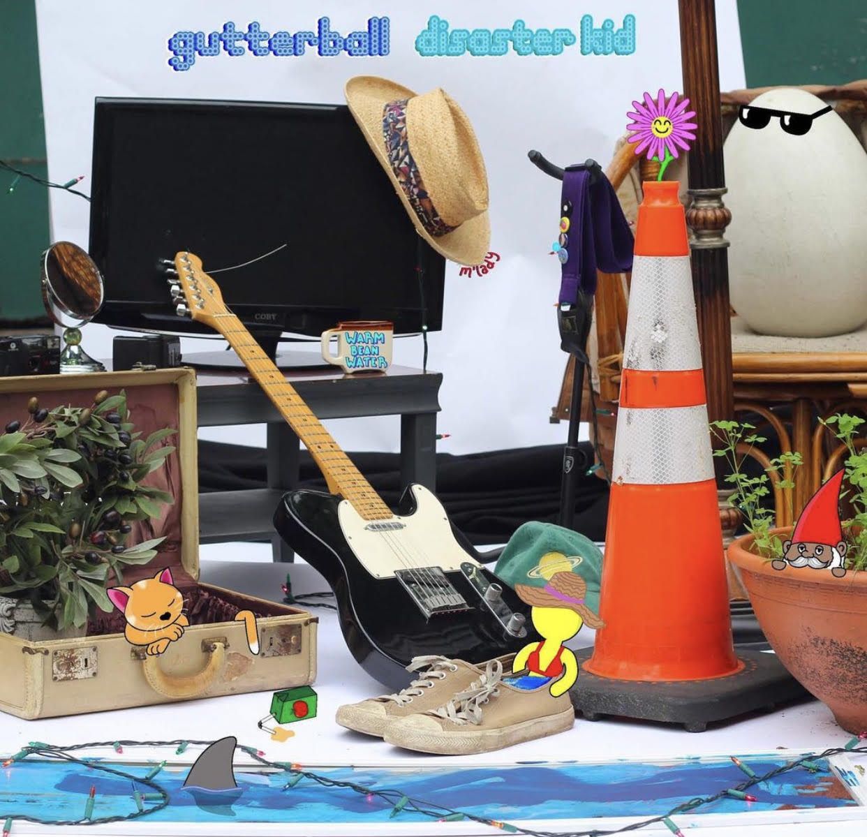 A guitar and a hat are on a table in front of a sign that says guitarball quarter lid
