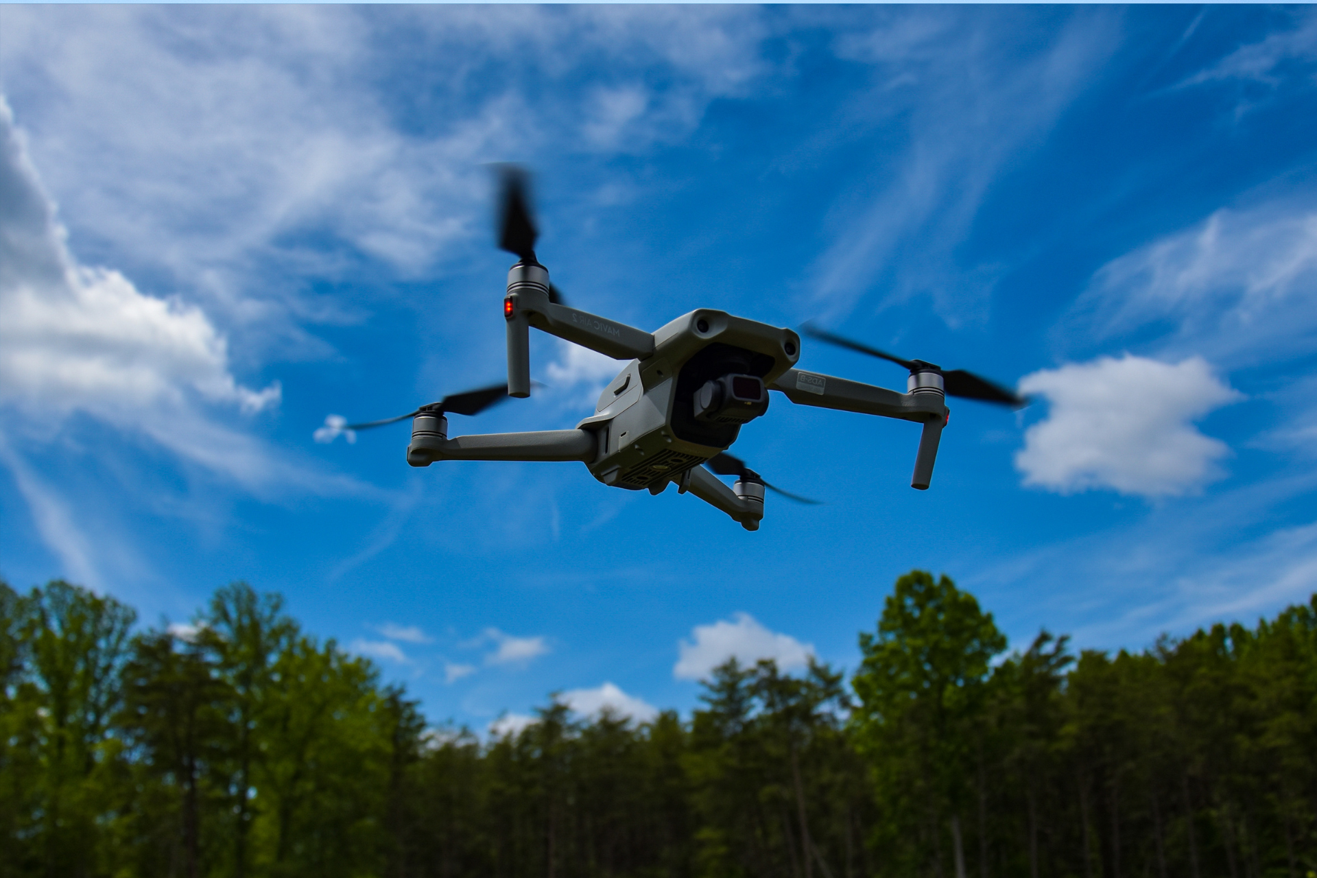 A drone is flying in the sky over a forest.