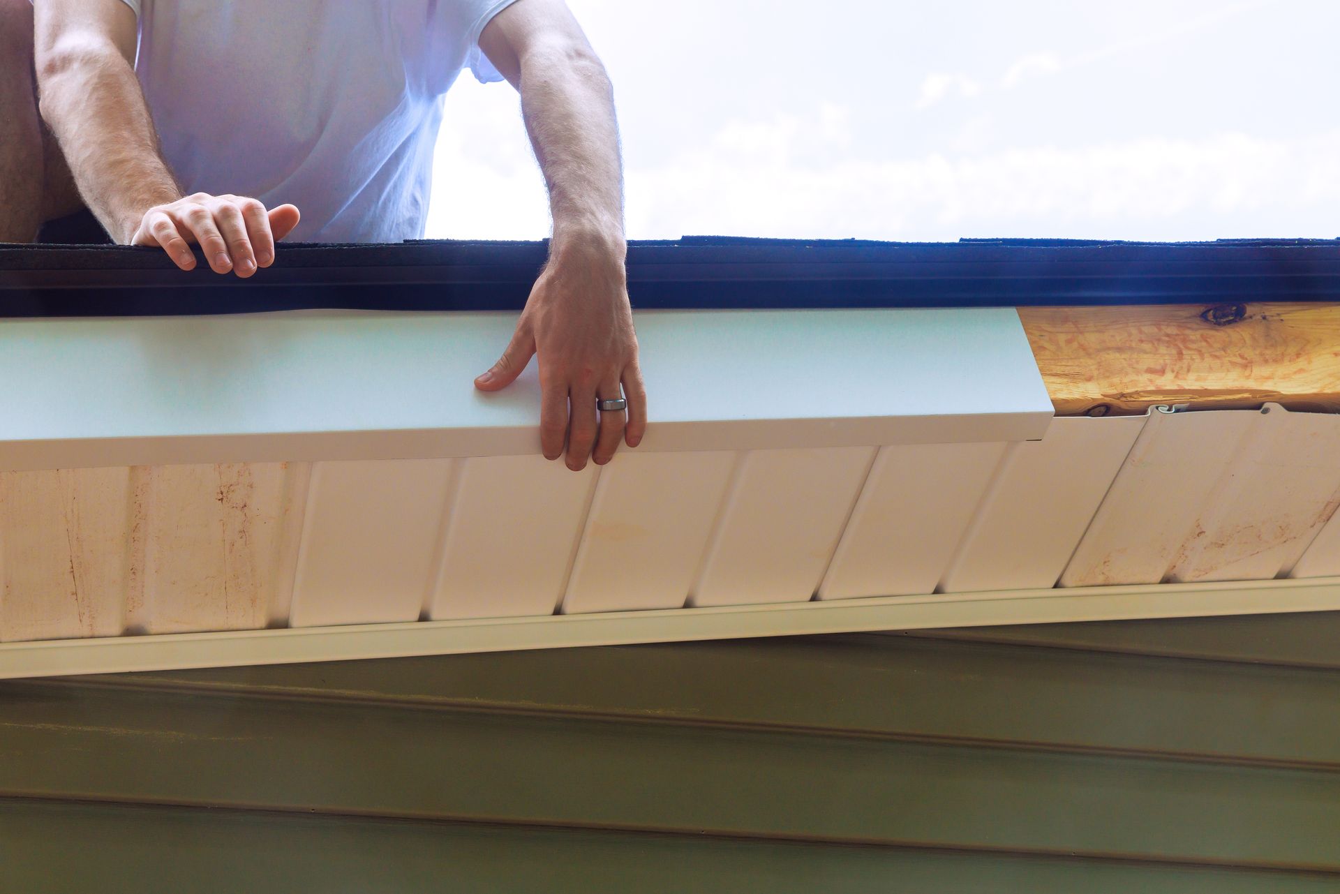 Person installs white trim on a house's eaves, holding a piece of it in place.
