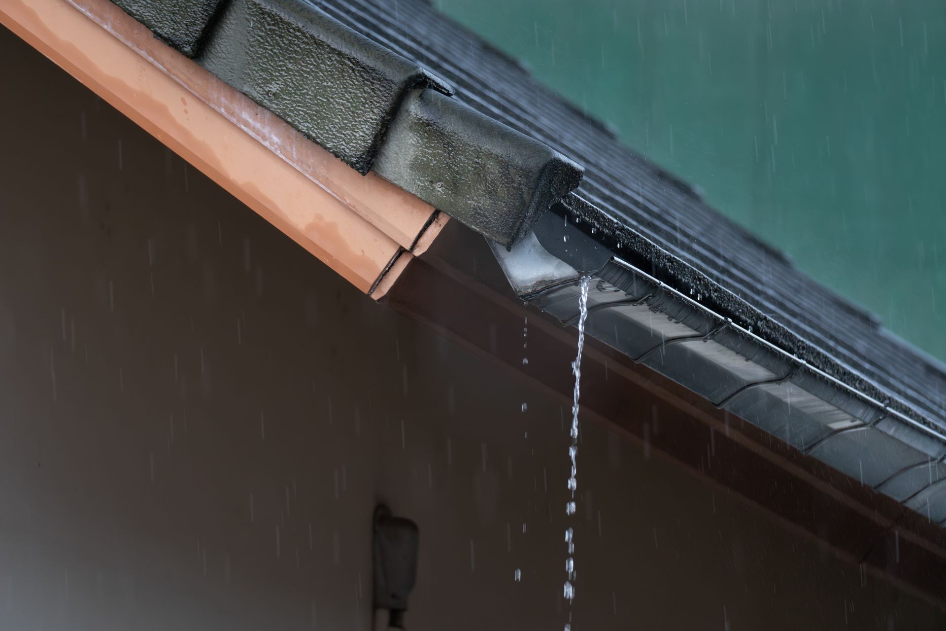 Rainwater pouring from a black gutter on a roof, brown fascia, and white exterior wall.