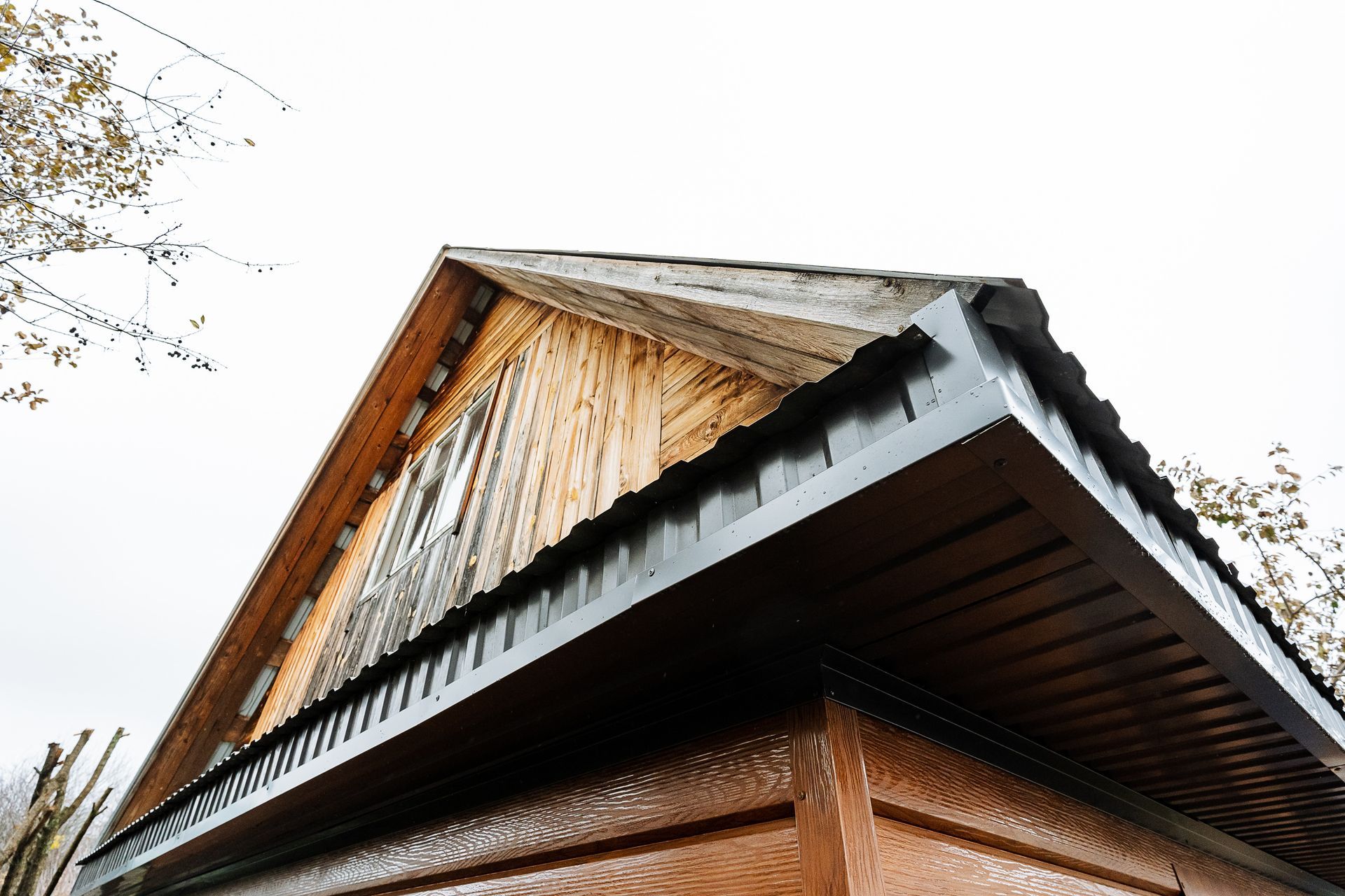 Wooden gable roof with dark brown trim and visible wood grain against a cloudy sky.