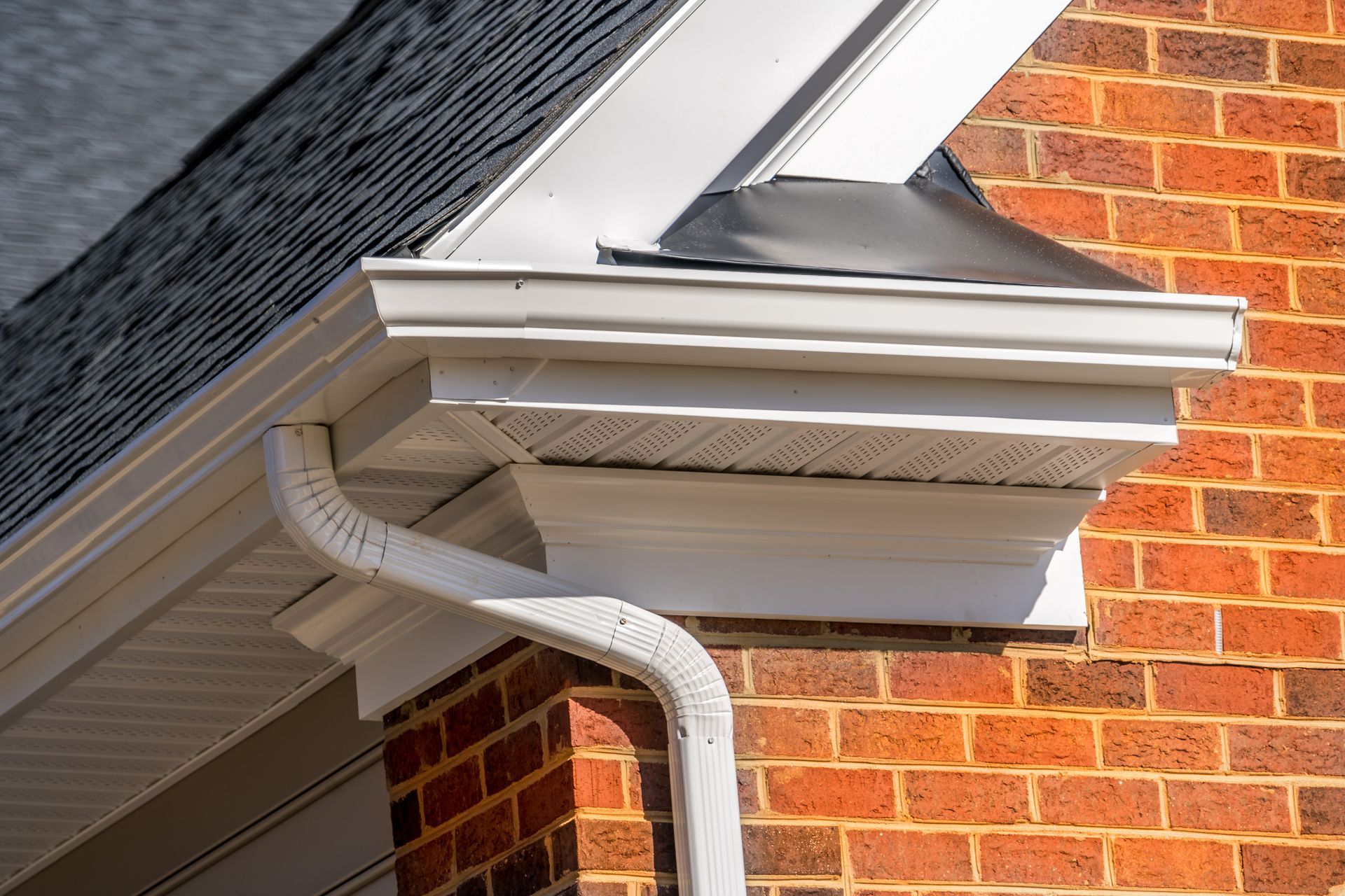 White gutter and trim on a red brick house with a dark roof.
