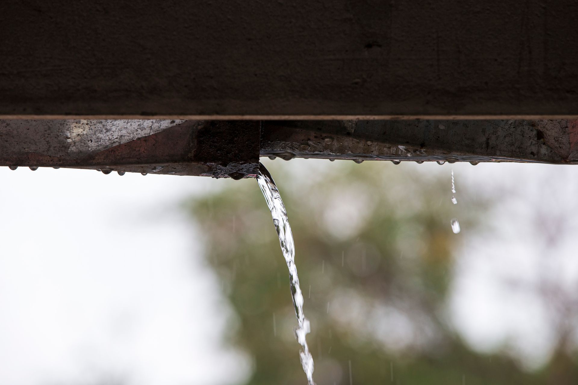 Water gushes from a damaged metal structure, with drips falling into the blurred background.