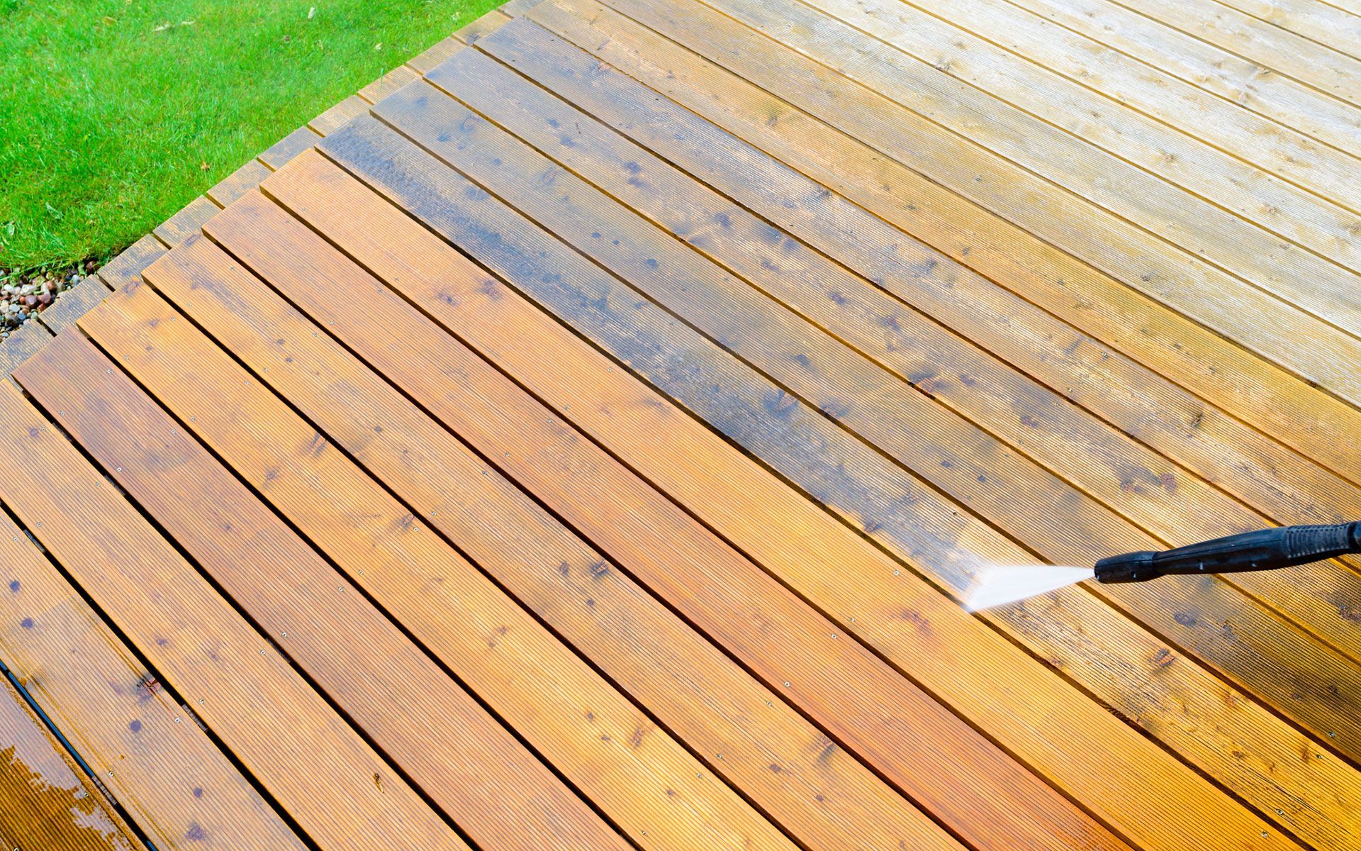 A person is cleaning a wooden deck with a high pressure washer.