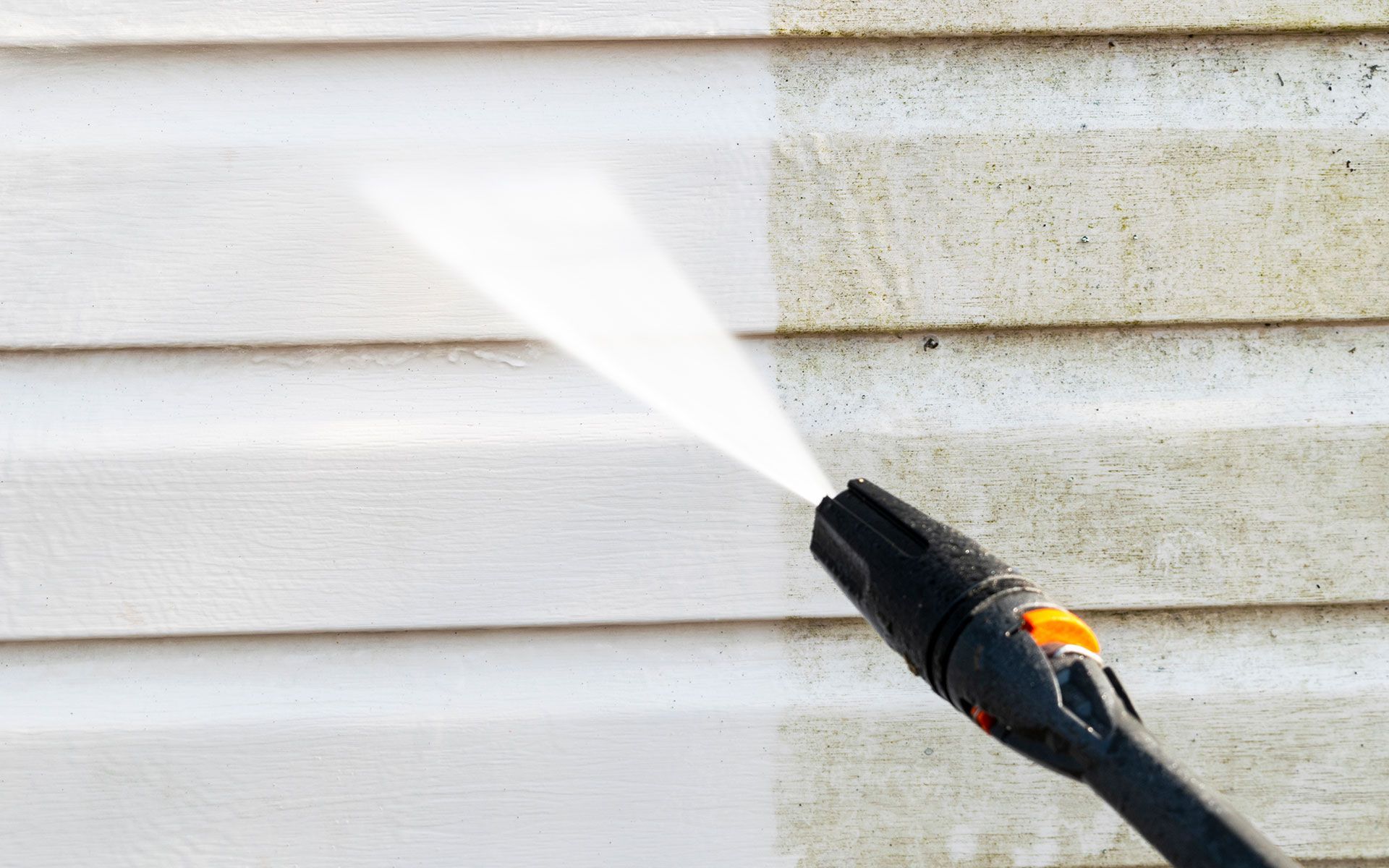 A person is cleaning the side of a house with a high pressure washer.